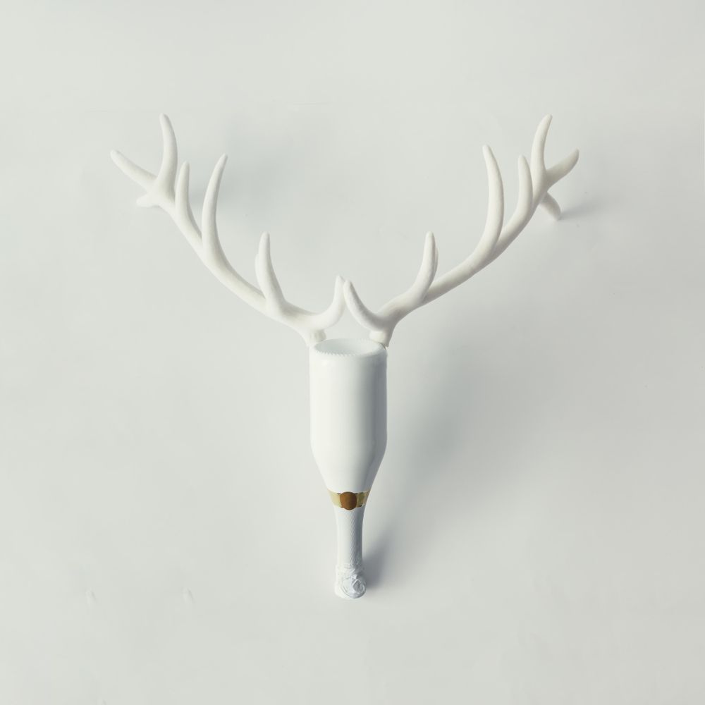 Champagne bottle with reindeer antlers with baubles on bright background