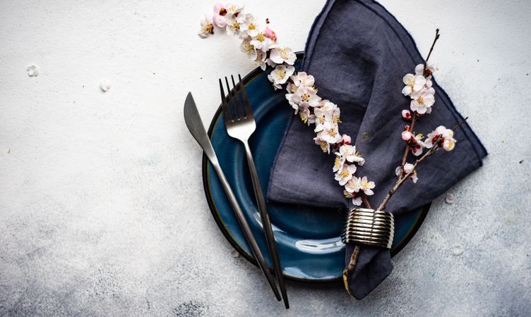 Table setting with delicate apricot blossom around elegant navy tableware on grey counter with space for text