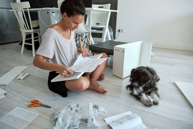 Focused woman reading furniture assembly instruction near dog