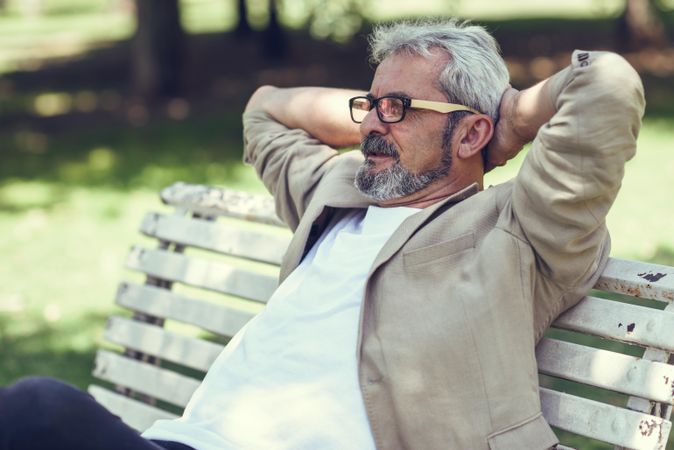 Mature man, sitting back on bench in a park with arms behind head
