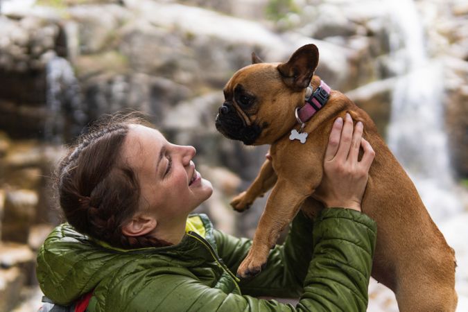 Cheerful traveling woman with dog near waterfall in forest