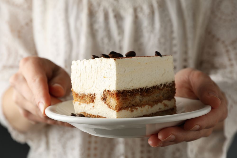 Girl holds plate with delicious tiramisu, close up. Selective focus