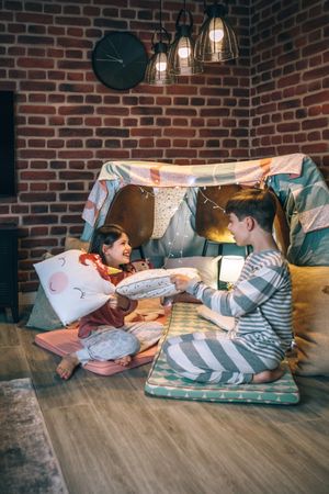 Happy children with pajama having fun in a pillow fight on handmade shelter tent in living room