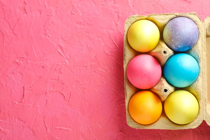 Decorative eggs in cardboard box on color background, space for text. Top view