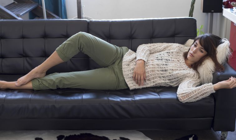 Female in wooly sweater reclining on leather couch in living room