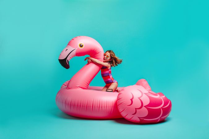 Girl in swimwear sitting on a giant inflatable pink flamingo.