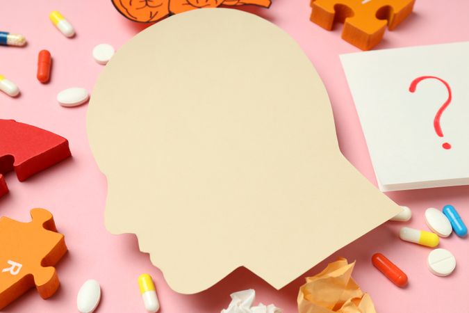 Close up of paper cut out of side view of head with medications and puzzle pieces on pink background
