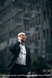 Smiling businessman talking over cell phone standing outdoors with a hand in pocket 4jnAx4