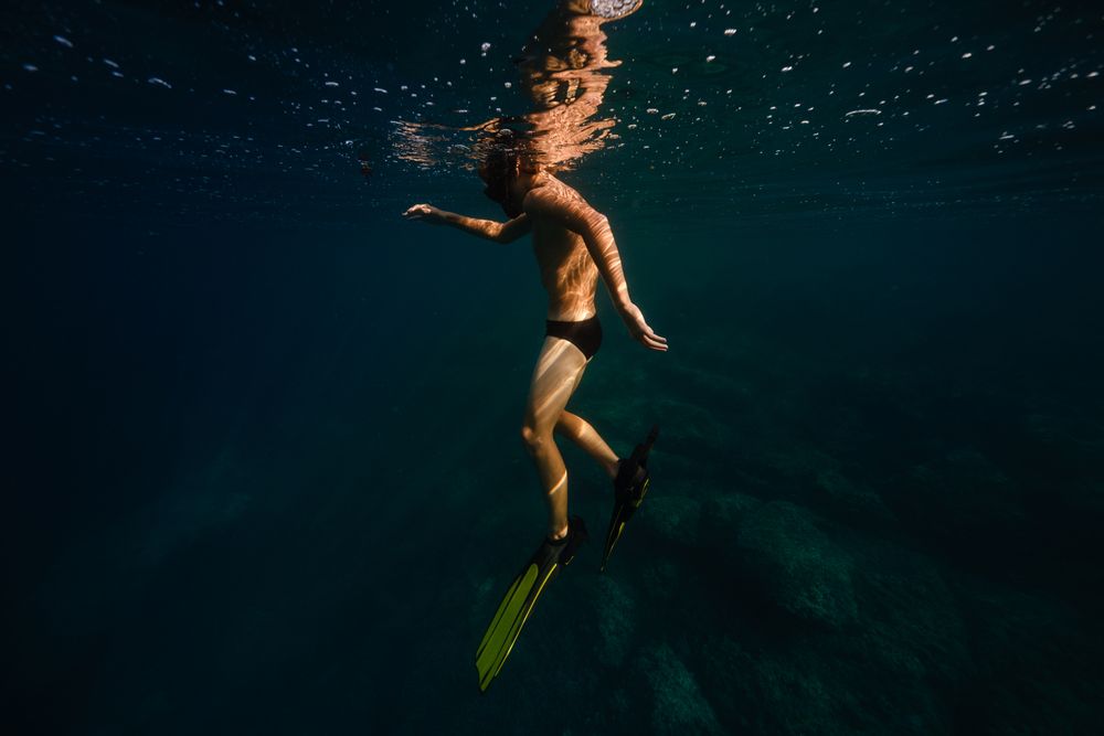 Anonymous male tourist diving undersea in sunlight