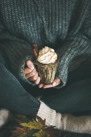 Woman in cozy sweater, socks and jeans holding whipped cream topped drink