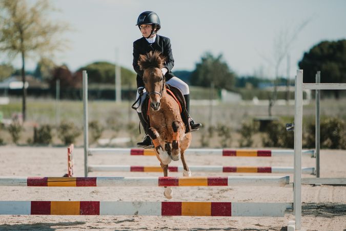 Teen girl riding horse and jumping over bars