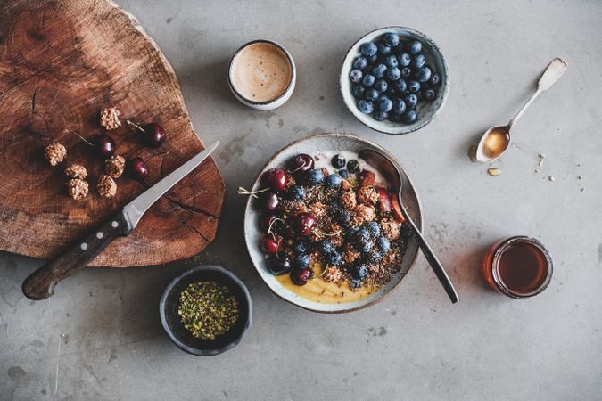 Oat granola yogurt bowl with cherries, blueberries, honey, nuts, coffee, wooden board