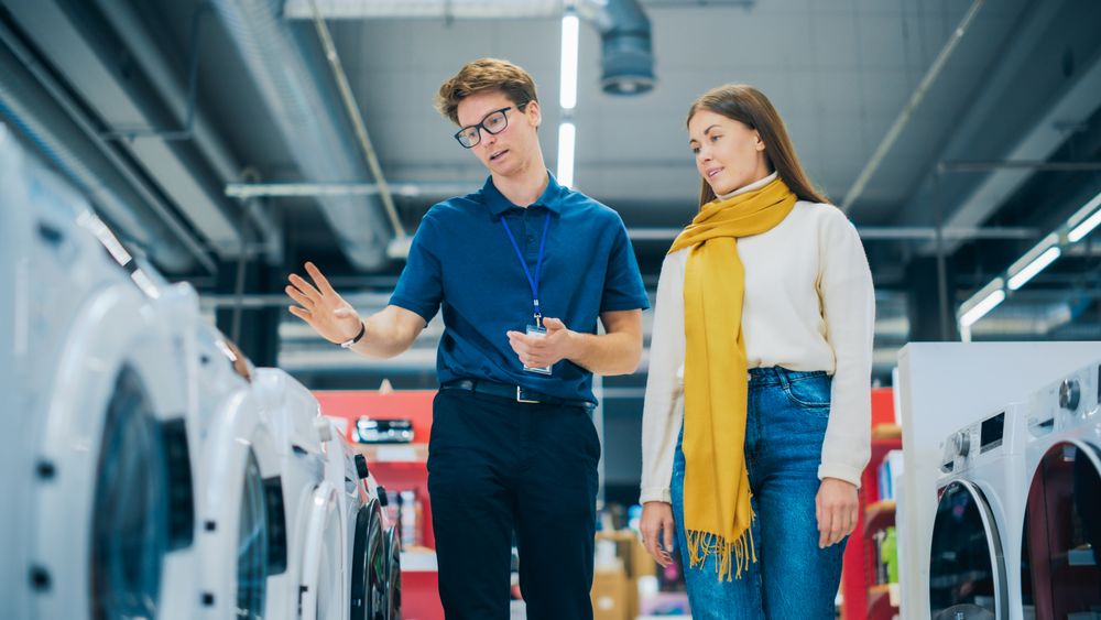 Portrait of a Retail Electronics Shop Consultant Assisting Young Female Customer in Selecting a Washing Machine.