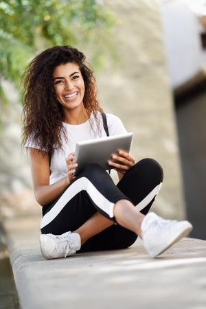 Laughing Arab woman with her digital tablet sitting outdoors, vertical