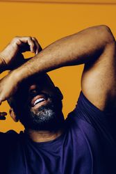 Exasperated Black man in yellow studio with arms over his eyes