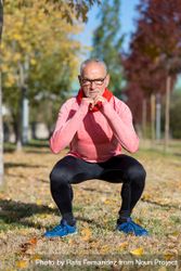 Grey haired man with glasses doing squats in the park 0yRVL5