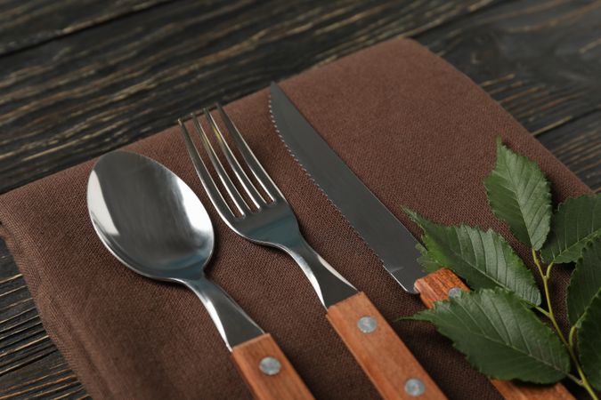 Napkin, fork, spoon, knife and leaf on wooden background