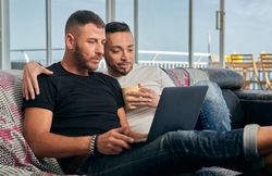 Happy gay couple using laptop at home