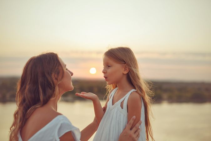 Little girl blowing a kiss to woman at sunset in front of lake