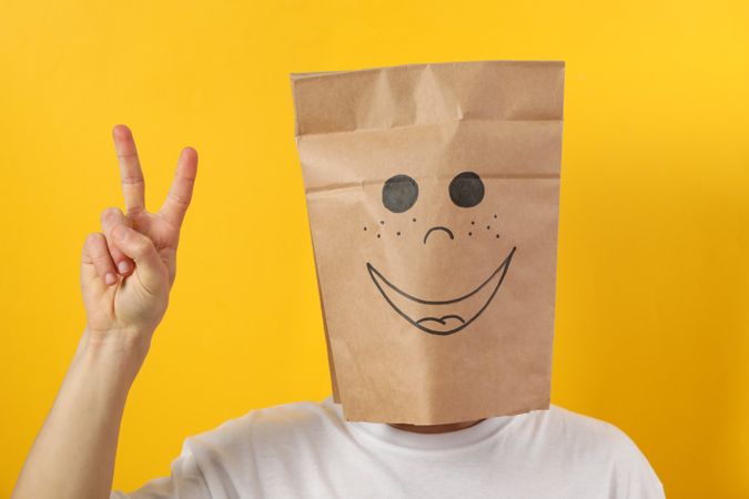 Person making peace sign with hands with paper bag on his head