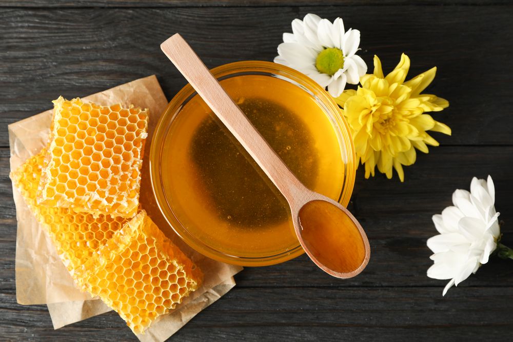 Honey, chrysanthemum and chamomile flowers on wooden background, top view