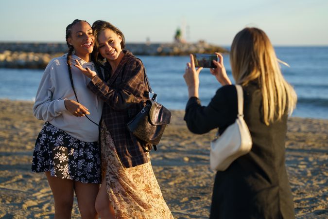 Smiling female friends hanging out taking pictures on beach at magic hour