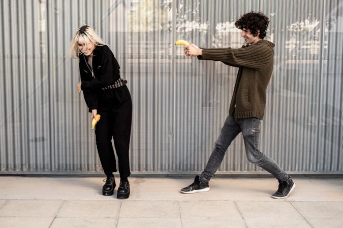 Happy couple pretending to shoot with bananas on street