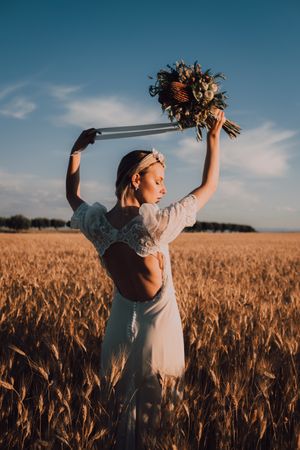 Charming woman in dress with open back raising hands with flower bouquet