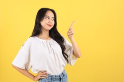Cheerful Young Asian Teenager Woman Smiling Confidently While Pointing to the Side with Her Index Finger