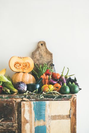 Fresh autumnal produce on kitchen counter, with halved squash and wooden board, vertical composition