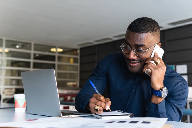 Black man talking on phone near laptop in office
