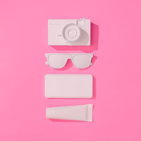 Summer objects of sunglasses, camera, smart phone and sunscreen on pink background