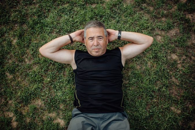 Cheerful older man doing abs on green grass in park