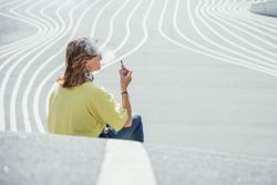 Modern relaxed woman vaping while sitting on marked road