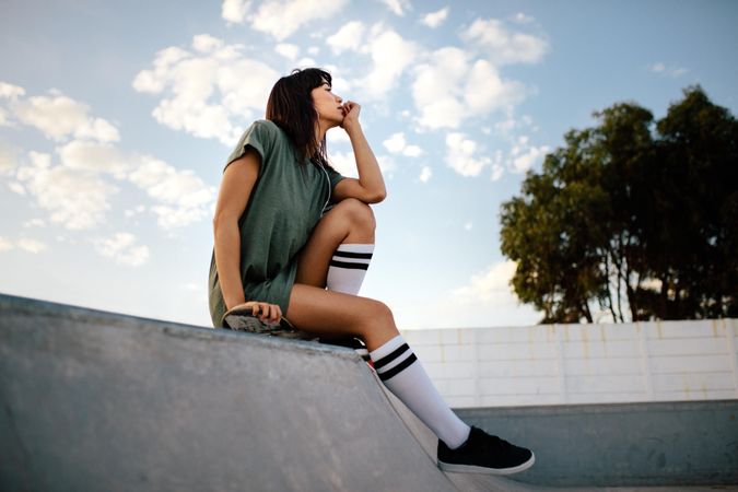 Young female skateboarded relaxing and thinking at skate park
