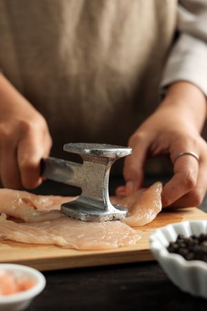 Hands of cook tenderizing chicken breast with meat mallet