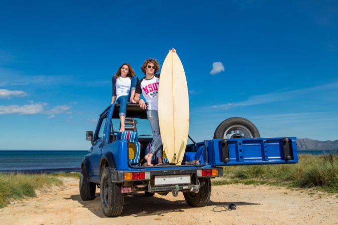Guy with surfboard and woman on roof of car