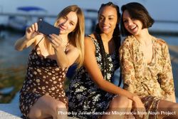 Three happy women sitting near coast taking selfie 5z1oA0