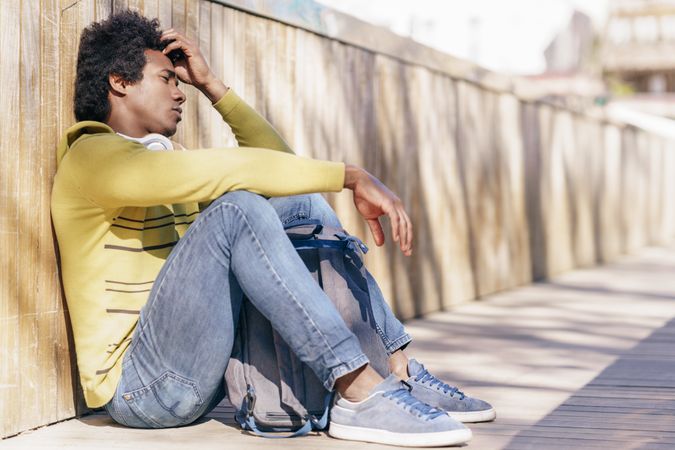 Man sitting against wall outside looking sad