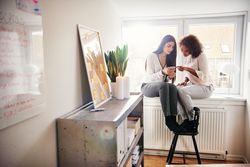 Two women in a modern office sitting on the window sill
