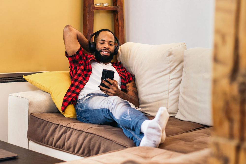 Black man relaxing using smartphone on the sofa at home