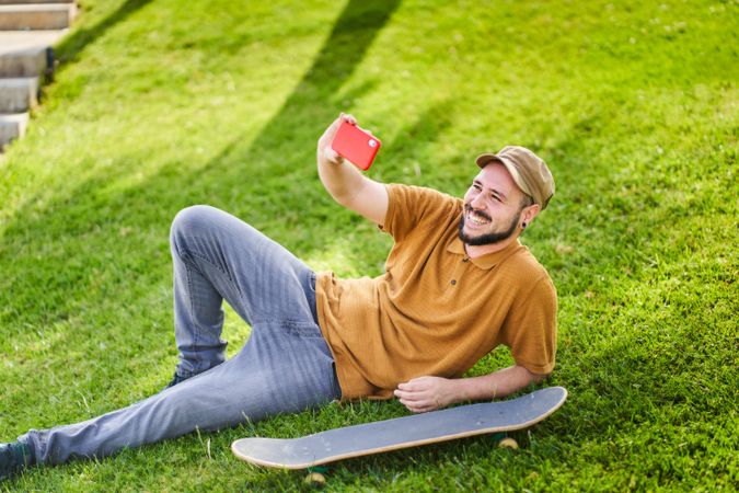 Man in cap relaxed smiling lying on the grass using his smartphone