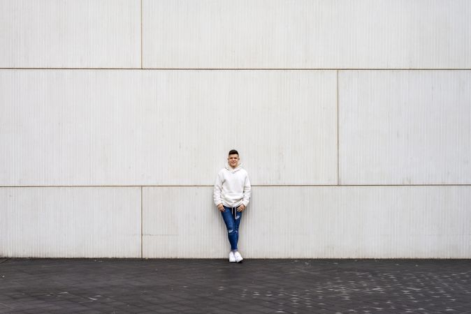 Young man in bright hoodie leaning on wall outside with copy space