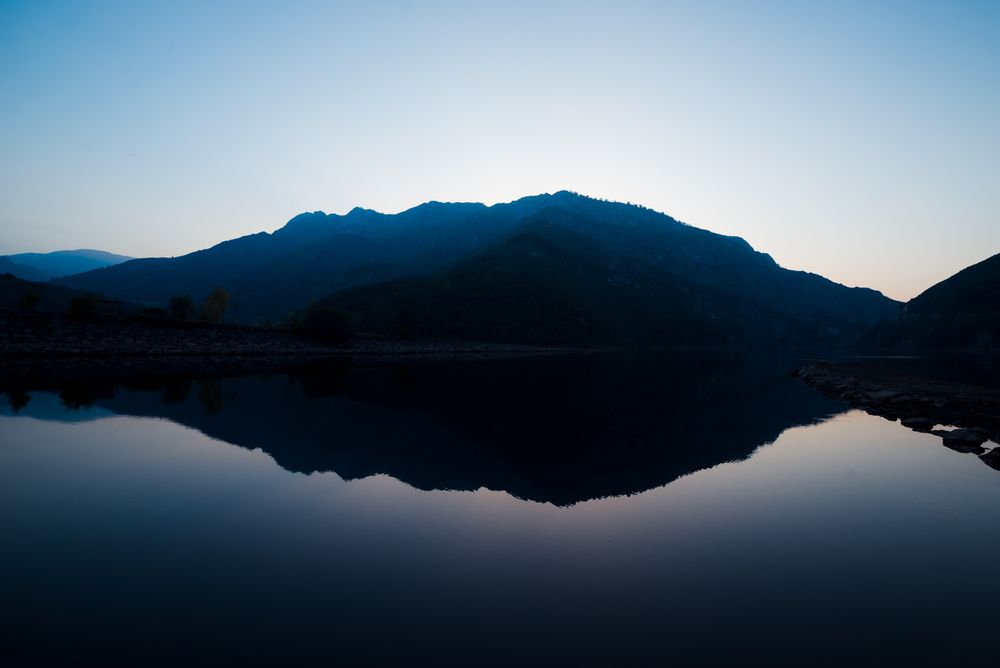 Picturesque view of water surface near amazing rock hills at sunset and blue sky