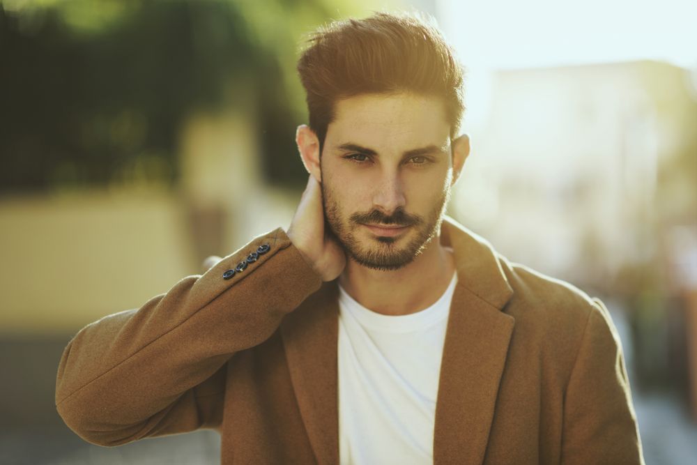 Bearded male in winter jacket walking outside with sun in background