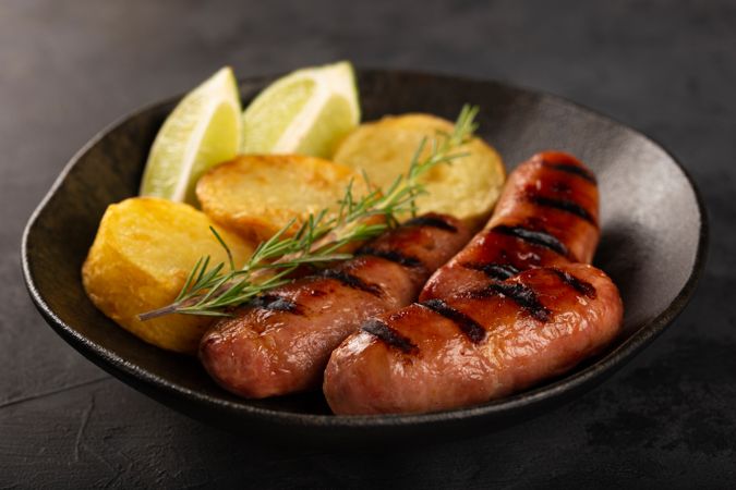 Plate with grilled sausages, potatoes, lime slices and sprig of rosemary