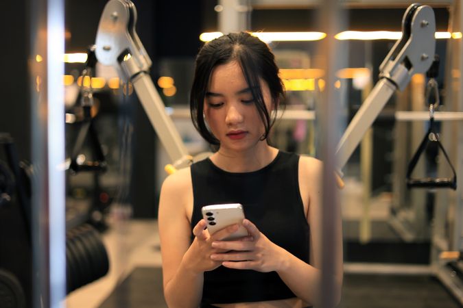 Young Female Sitting on Bench at the Gym with Mobile Phone