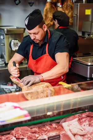 Butcher cutting cured ham  with knife