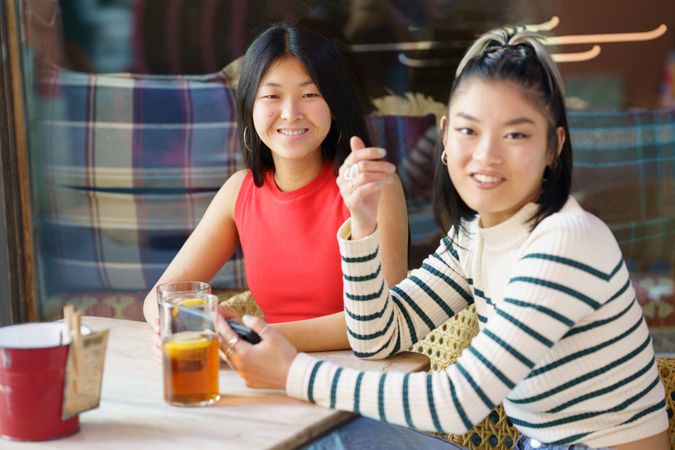 Two women sitting in restaurant patio with drinks looking at camera