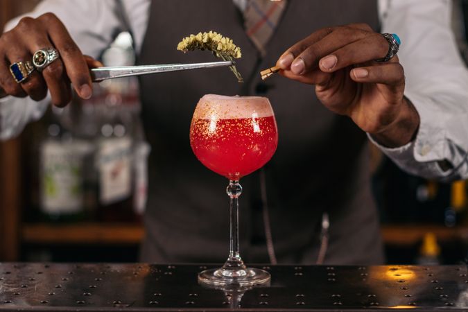 Close-up of an unrecognizable Black bartender pouring a cocktail and decorating it with garnish